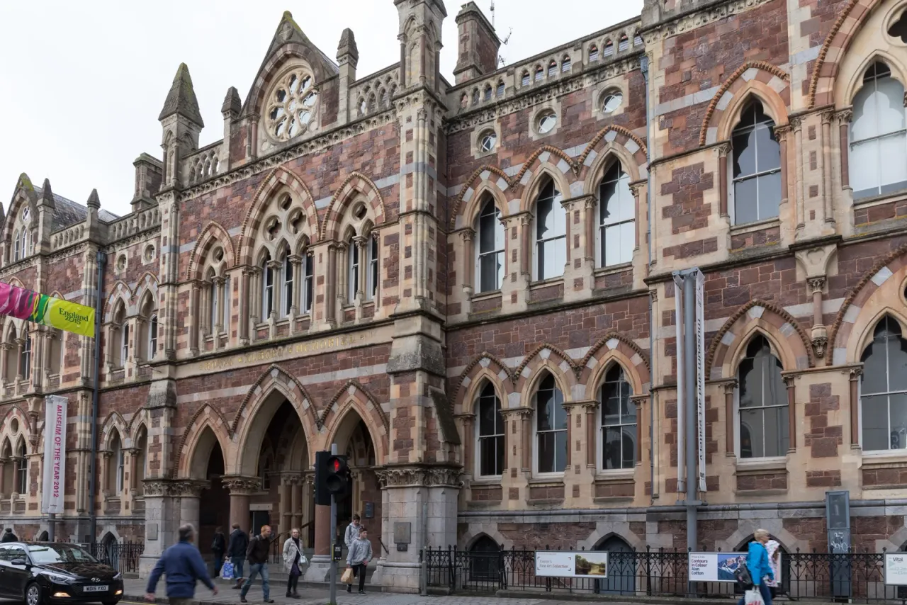 Neogotycka elewacja Royal Albert Memorial Museum & Art Gallery przy Queen Street w Exeter, wzniesiona z wielobarwnego kamienia, z ostrołukowym wejściem i przechodniami na chodniku
